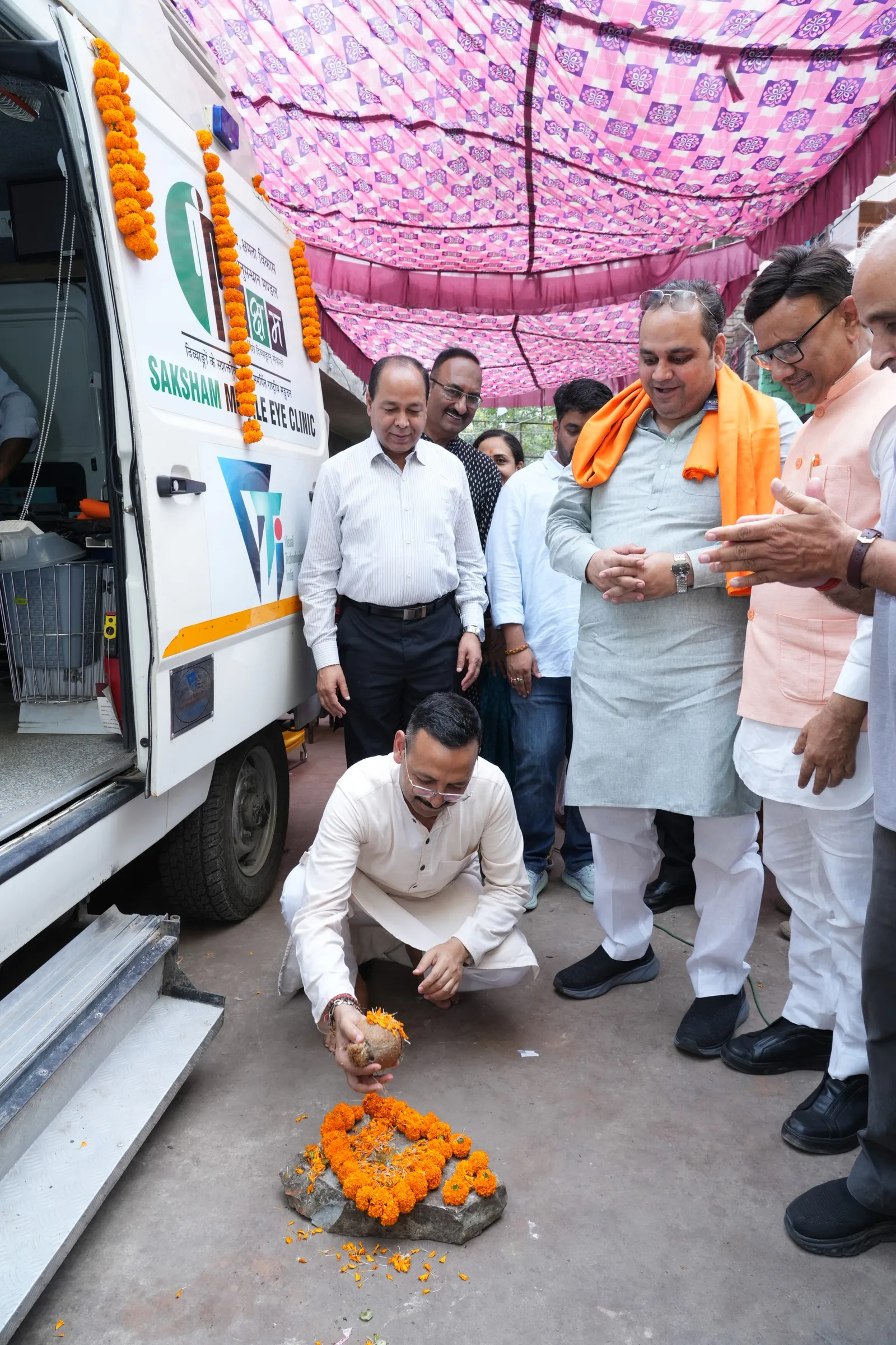 A guest offers marigold flowers at a small puja beside the mobile eye clinic as others look on.