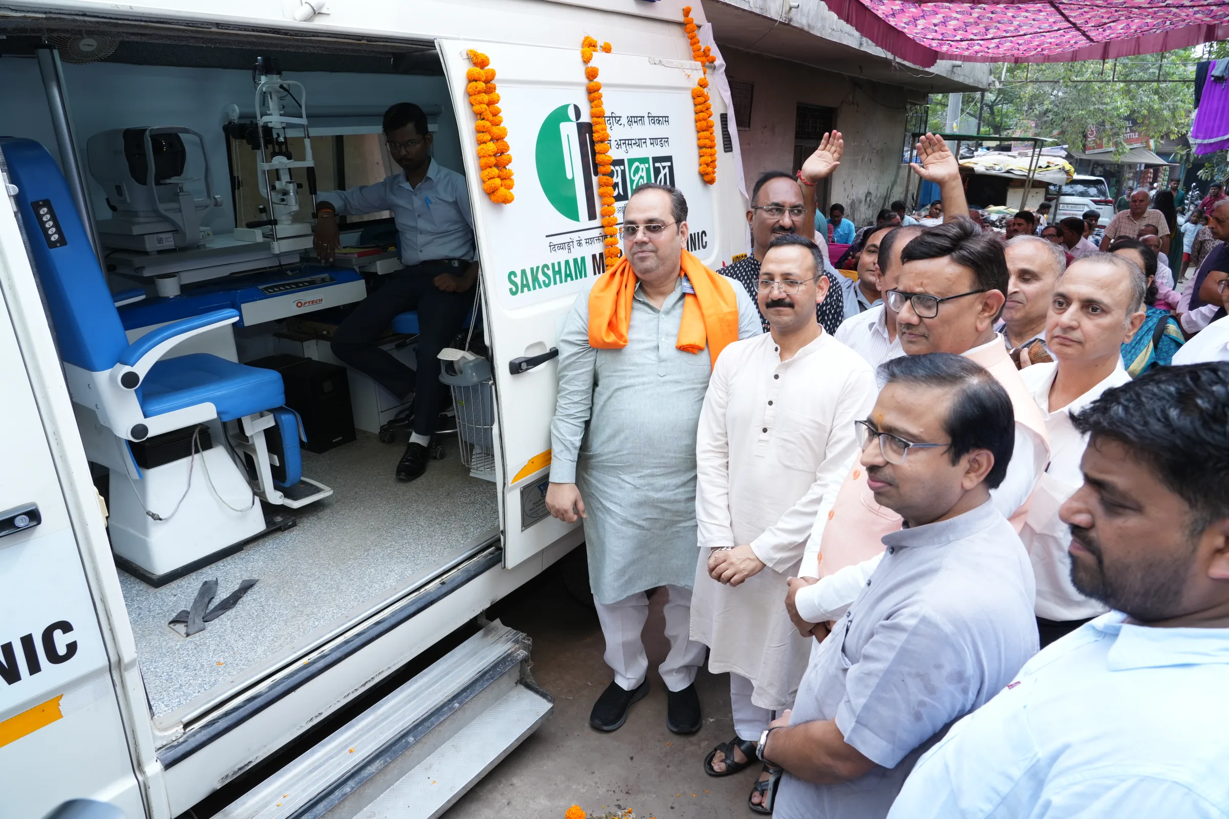 Guests gathered at the open door of the Saksham mobile eye clinic van, with eye-testing equipment visible inside.