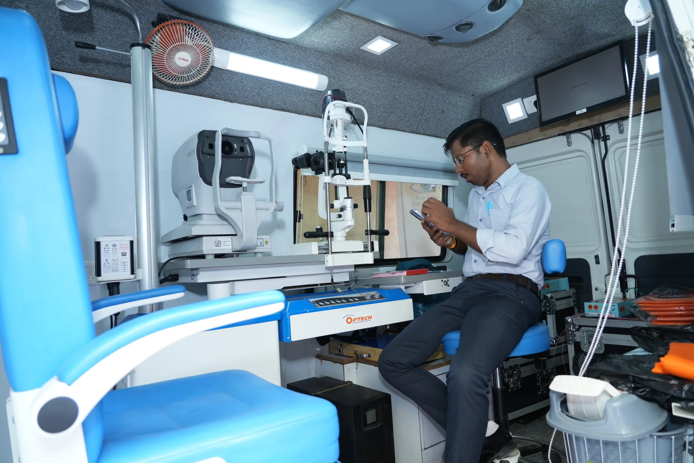 Inside the mobile eye clinic: a patient chair and eye-examination instruments, with a staff member seated at the desk.